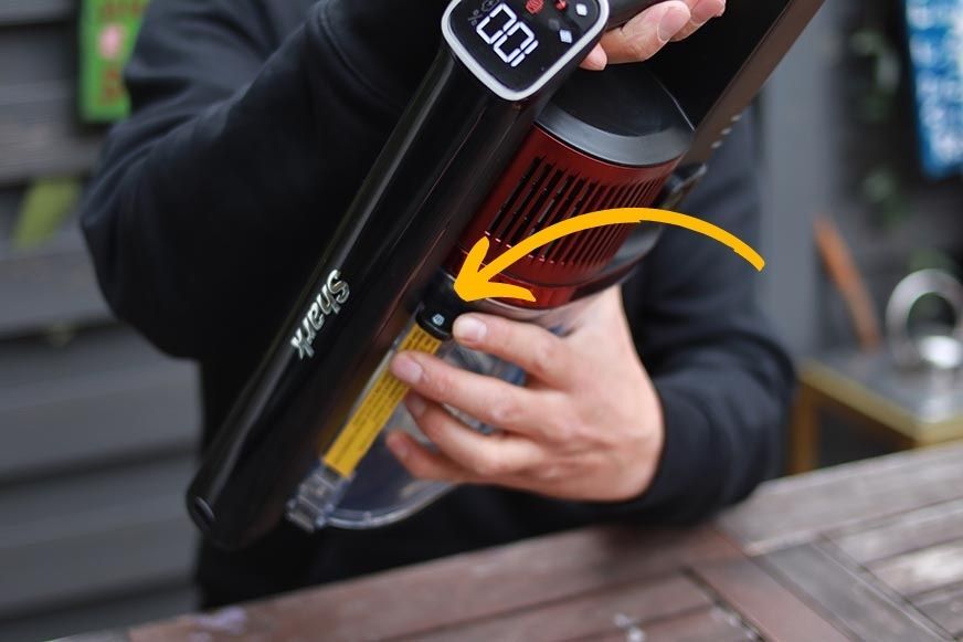 Man sieht den Knopf, um den Schmutzbehälter des Shark Anti Hair Wrap Flexology abzunehmen.